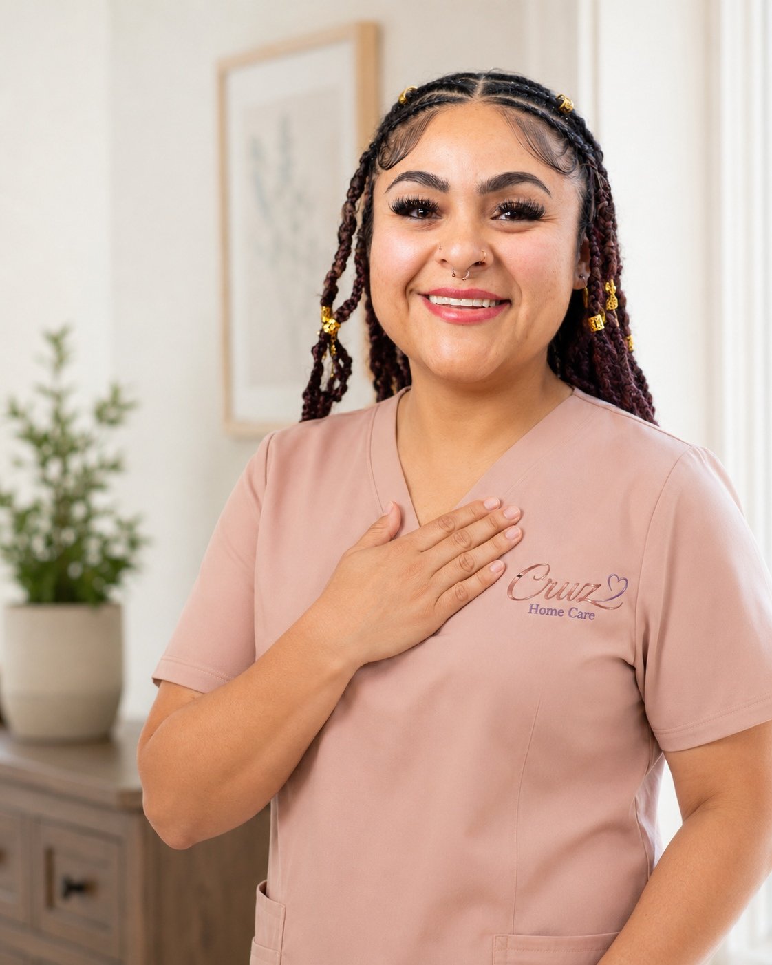 A smiling Cruz Home Care caregiver with long braided hair in rose-gold scrubs